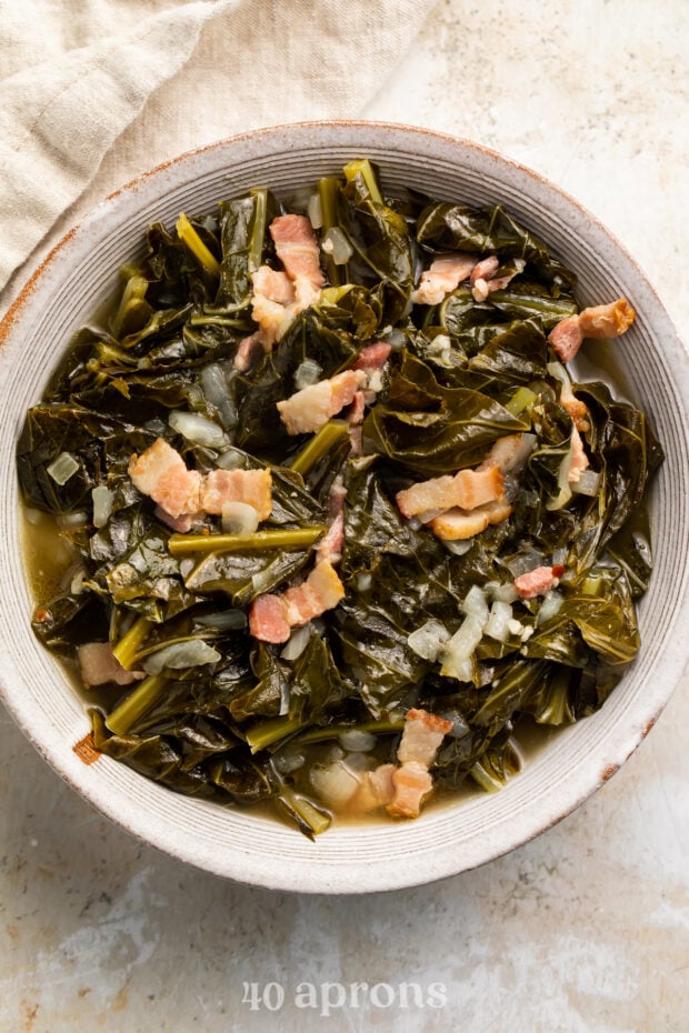 Overhead view of a white bowl of Instant Pot collard greens with bacon on a neutral tabletop.