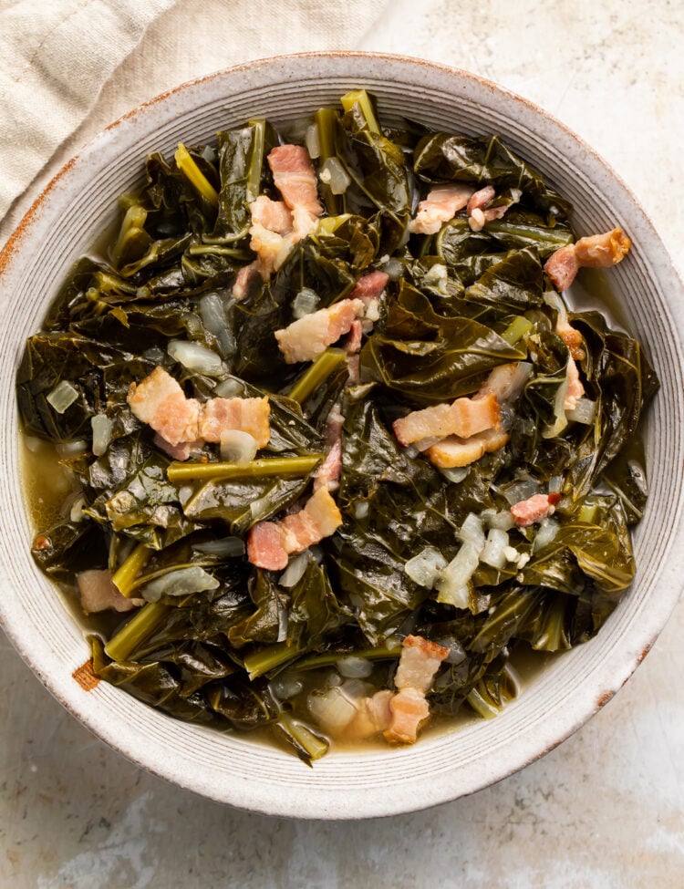 Overhead view of a white bowl of Instant Pot collard greens with bacon on a neutral tabletop.