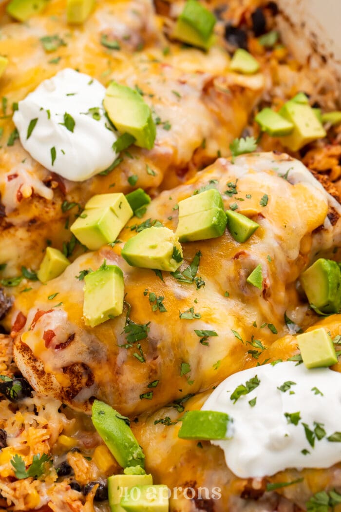 Close-up view of a chicken breast from a Mexican chicken and rice casserole topped with sour cream and avocado.