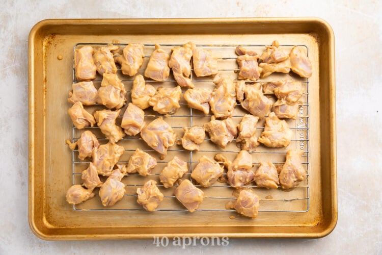 Overhead view of marinated Thai peanut chicken pieces on a wire baking rack on a gold baking sheet.