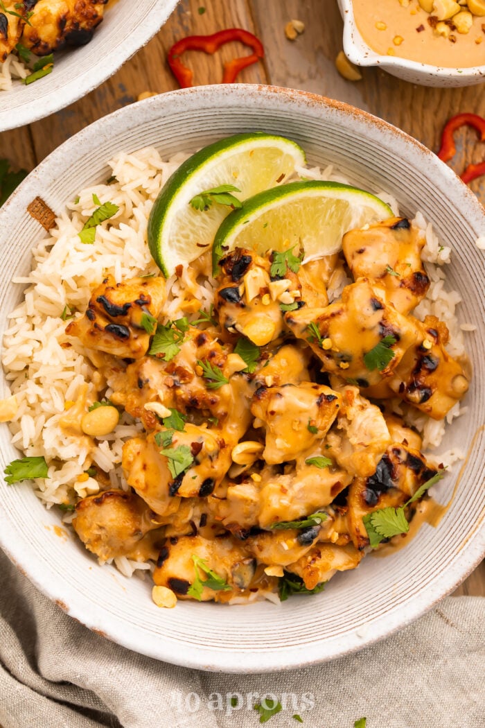 Overhead view of a bowl of Thai peanut chicken and rice with lime wedges.