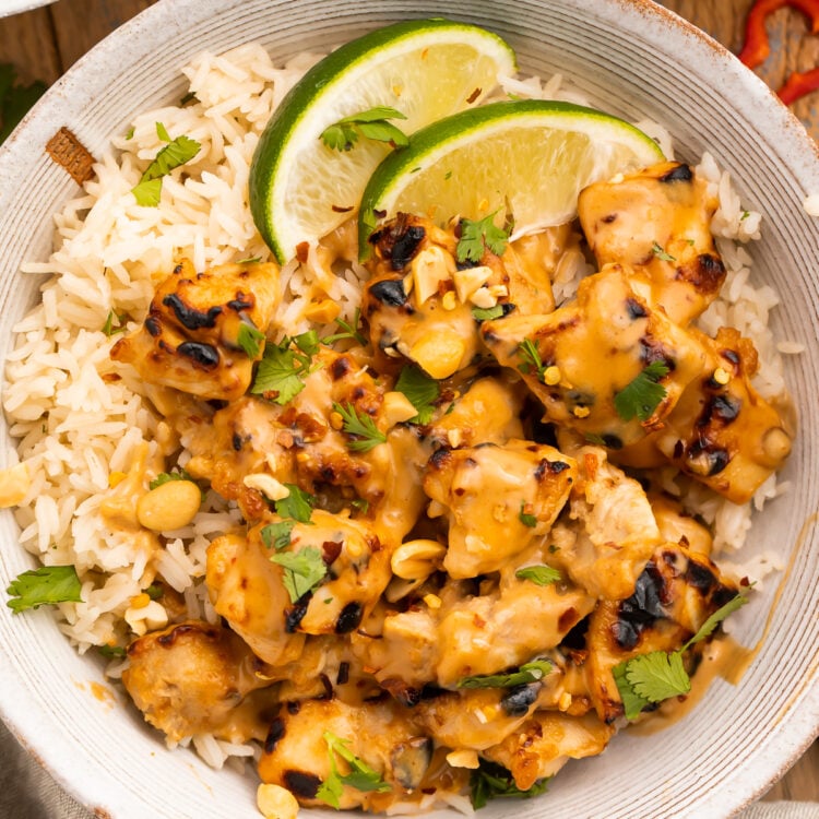 Overhead view of a bowl of Thai peanut chicken and rice with lime wedges.