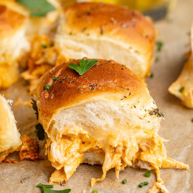 Side view, close up on one buffalo chicken slider, overflowing with melty cheese and shredded buffalo chicken.