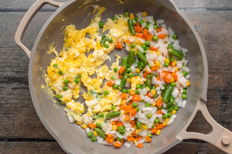Overhead view of frozen peas and carrots in a large skillet with scrambled eggs.