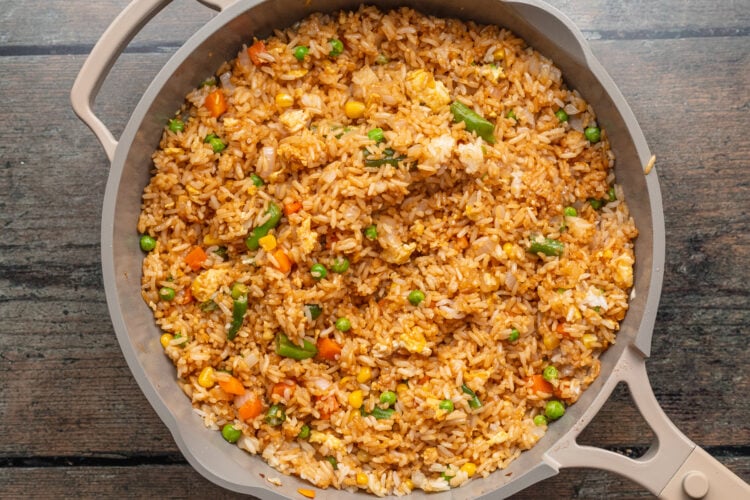 Overhead view of fried rice with peas, carrots, onions, and scrambled eggs in a large grey skillet.