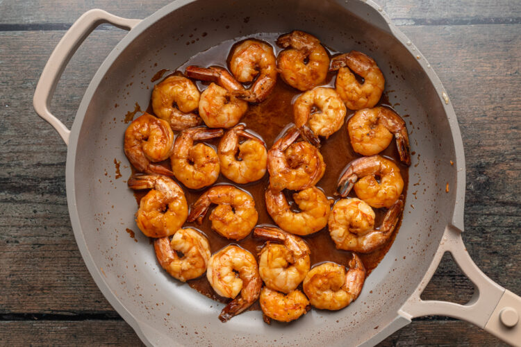 Overhead view of bright orange hibachi shrimp in a large grey skillet on a neutral background.