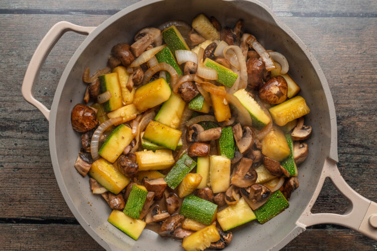 Overhead view of sautéed vegetables in a large grey skillet on a neutral background.