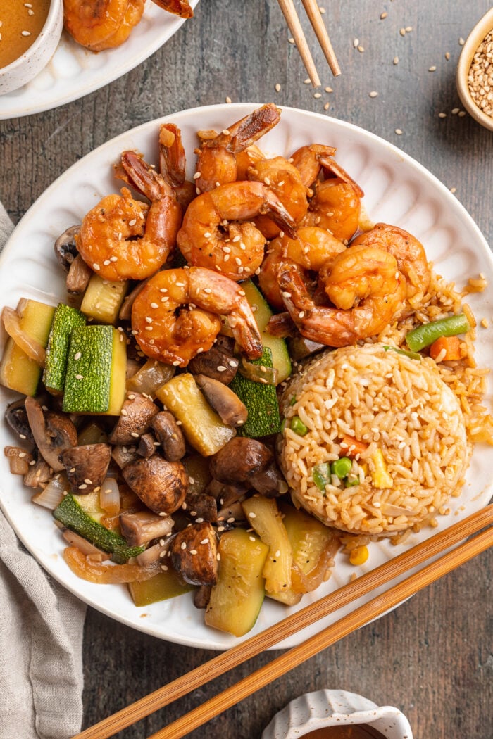 Overhead view of a plate of hibachi shrimp with sautéed veggies, fried rice, and chopsticks.