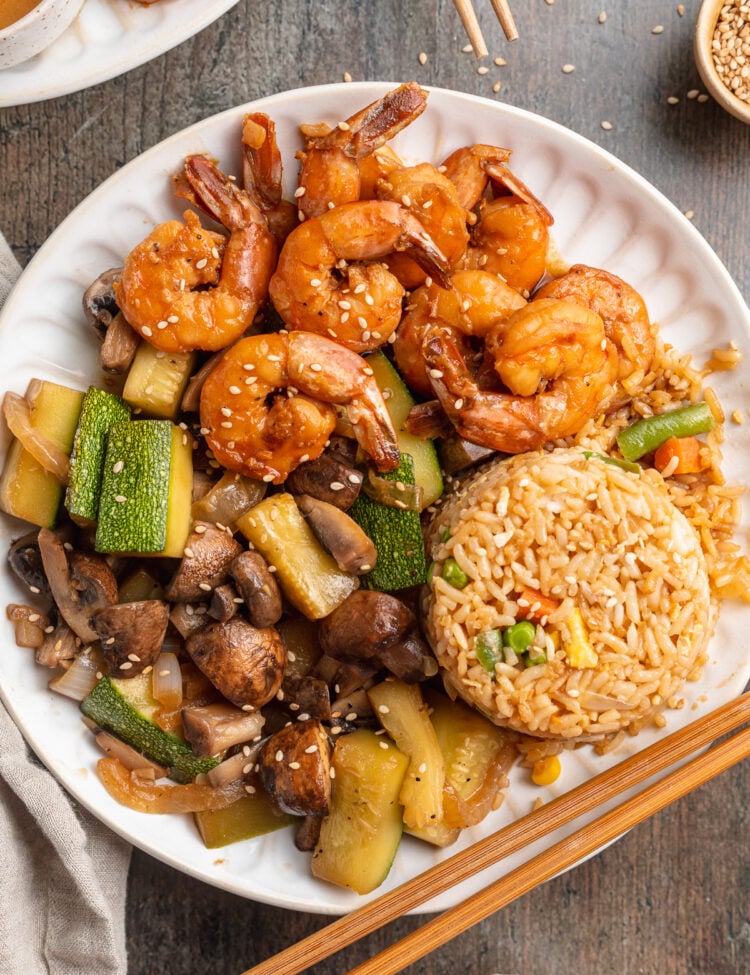 Overhead view of a plate of hibachi shrimp with sautéed veggies, fried rice, and chopsticks.