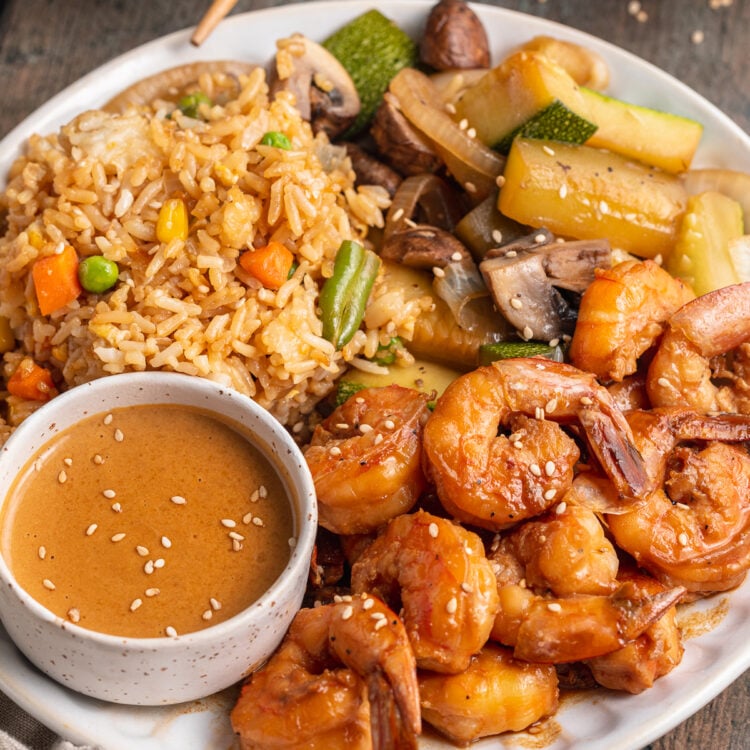 Angled view of hibachi shrimp with fried rice, sautéed vegetables, and a spicy mustard sauce on a plate.