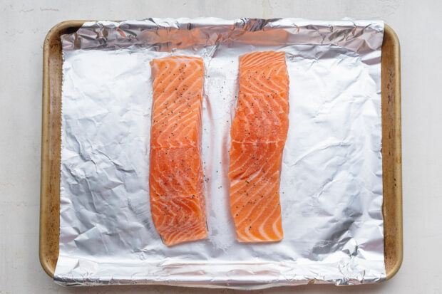 Overhead view of two salmon fillets on a baking sheet lined with aluminum foil.
