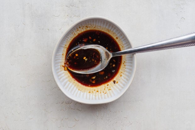 Overhead view of a ginger-garlic soy sauce mixture in a white bowl with a silver spoon.