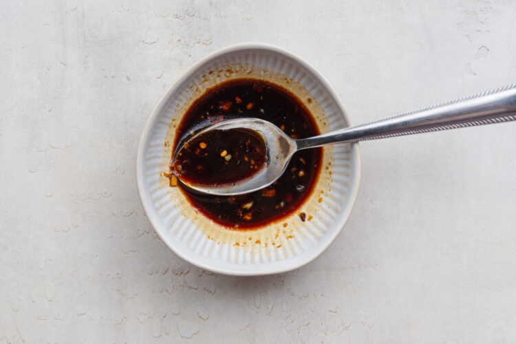 Overhead view of a ginger-garlic soy sauce mixture in a white bowl with a silver spoon.