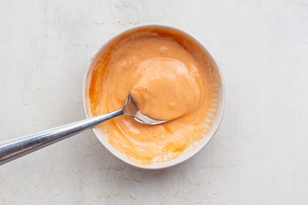Overhead view of prepared sriracha mayo in a white bowl with a silver spoon.