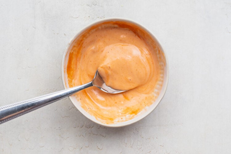 Overhead view of prepared sriracha mayo in a white bowl with a silver spoon.