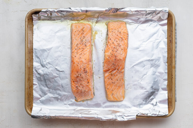 Overhead view of two fully-baked salmon fillets on a baking sheet lined with aluminum foil.