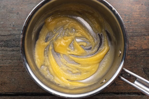 Overhead view of melted butter whisked with flour in a saucepan to create a roux.