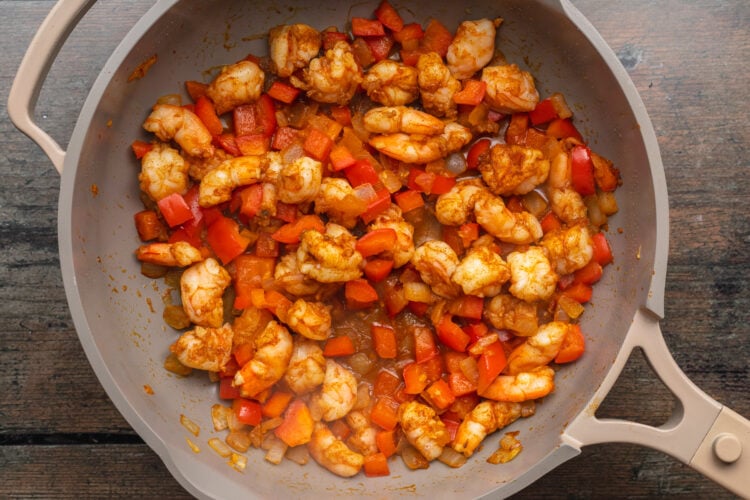 Overhead view of chopped shrimp in a large skillet with chopped onion and red bell pepper.