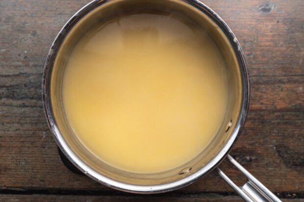 Overhead view of roux and chicken broth in a medium saucepan on a neutral background.