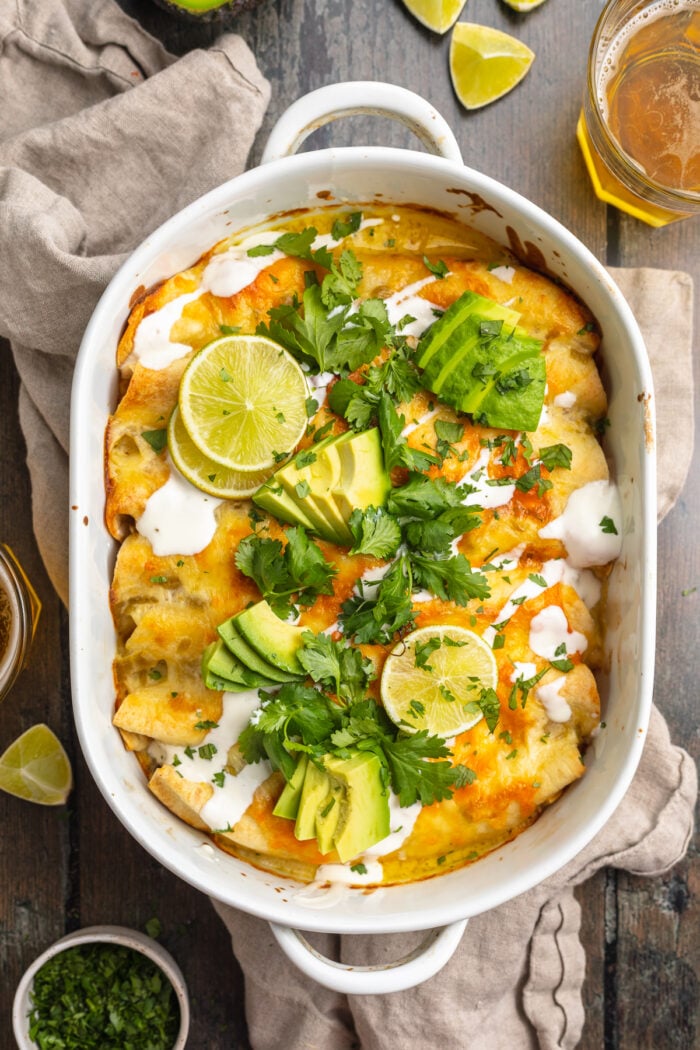 Overhead view of a casserole dish containing shrimp enchiladas topped with cilantro, slices of avocado, and sour cream.