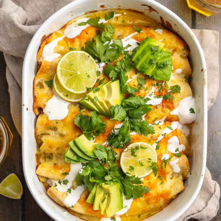Overhead view of a casserole dish containing shrimp enchiladas topped with cilantro, slices of avocado, and sour cream.