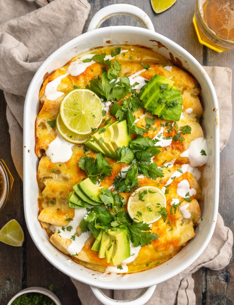 Overhead view of a casserole dish containing shrimp enchiladas topped with cilantro, slices of avocado, and sour cream.