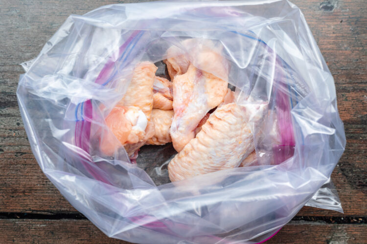 Overhead view of uncooked chicken wings in a large ziploc bag on a dark wooden tabletop.
