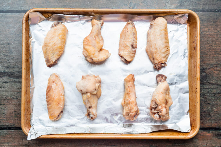 Overhead view of sous vide cooked chicken wings on a baking sheet lined with aluminum foil before the wings go under the broiler.