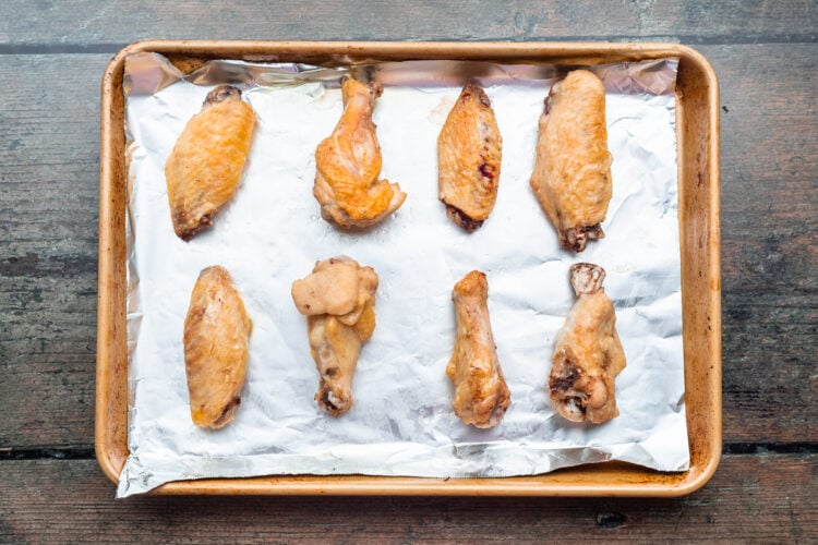 Overhead view of sous vide cooked chicken wings on a baking sheet lined with aluminum foil after the wings go under the broiler.