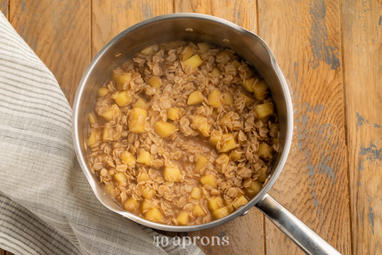 Overhead view of apple cinnamon oatmeal with chopped sweet apples in a medium silver saucepan on a neutral table.