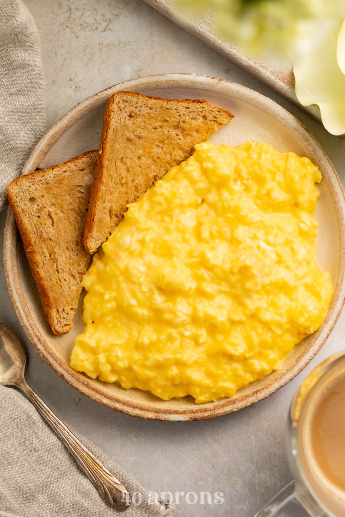 Overhead view of a bowl of mom's favorite cheesy scrambled eggs with two triangles of toasted whole grain bread.