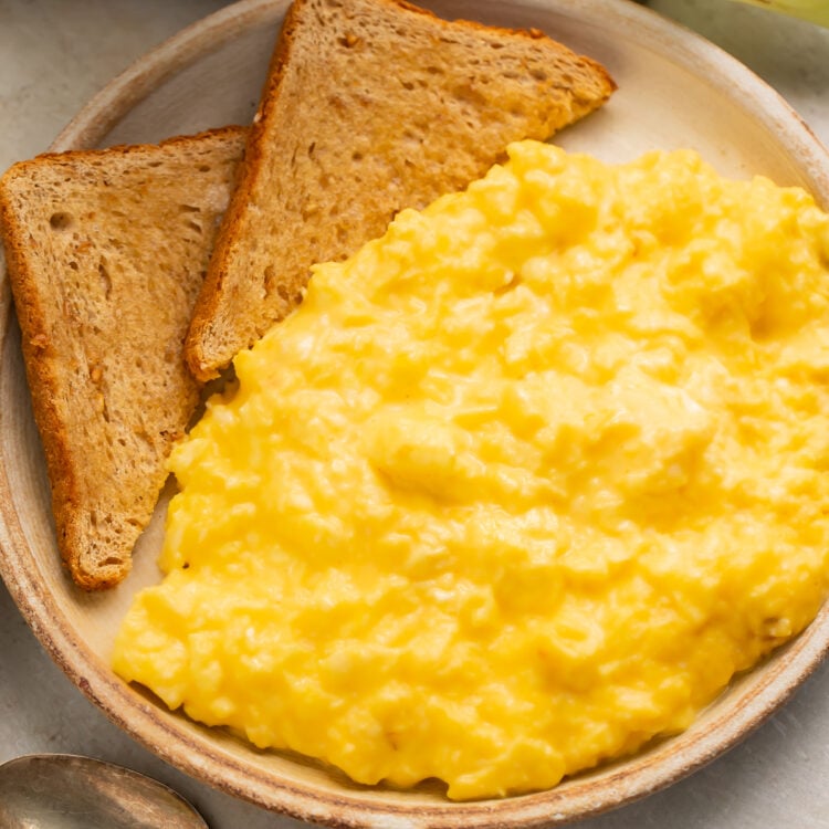Overhead, angled view of a bowl of mom's favorite cheesy scrambled eggs with two triangles of toasted whole grain bread.