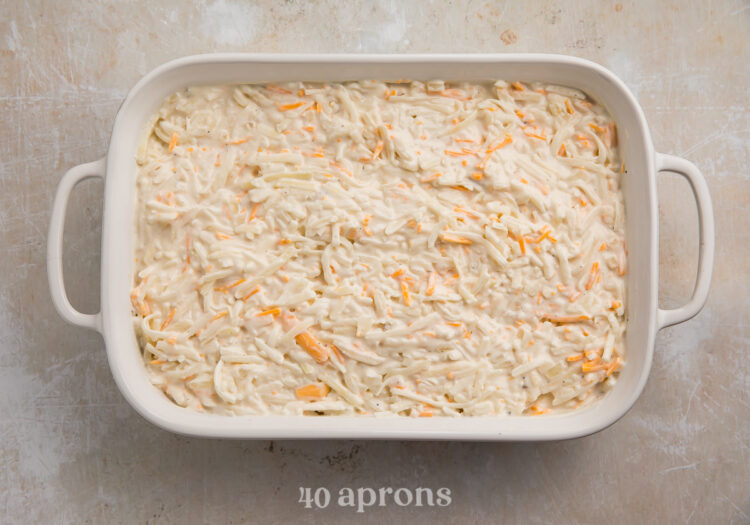 Overhead view of uncooked hashbrown casserole in a large white baking dish with handles.