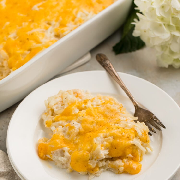 Closer, angled view of a scoop of Cracker Barrel hashbrown casserole topped with cheese on a white plate with a fork.