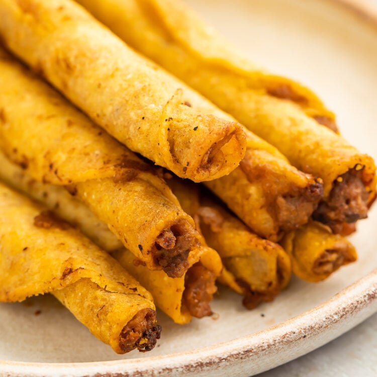 A stack of frozen taquitos cooked in the air fryer then arranged on a white plate in a pyramid-shaped pile.