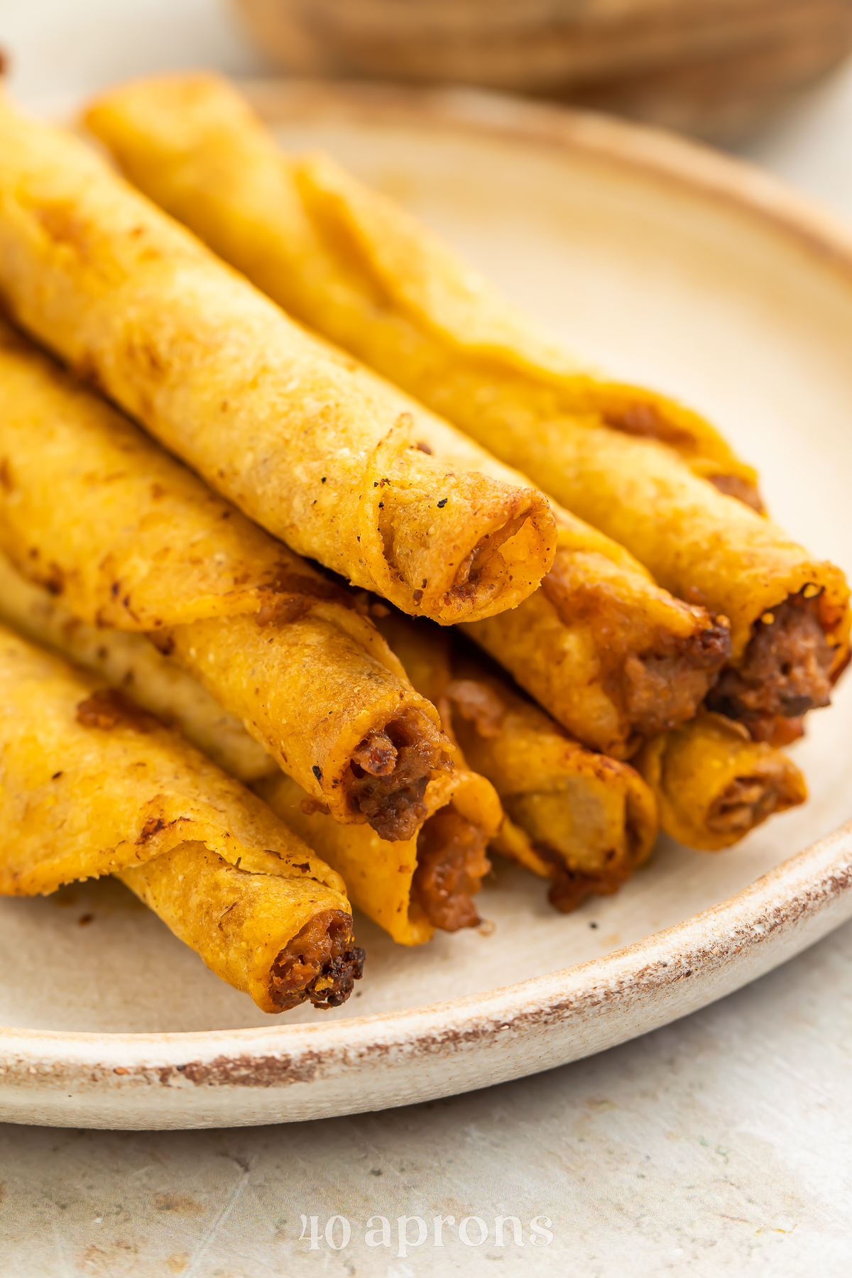 A stack of frozen taquitos cooked in the air fryer then arranged on a white plate in a pyramid-shaped pile.