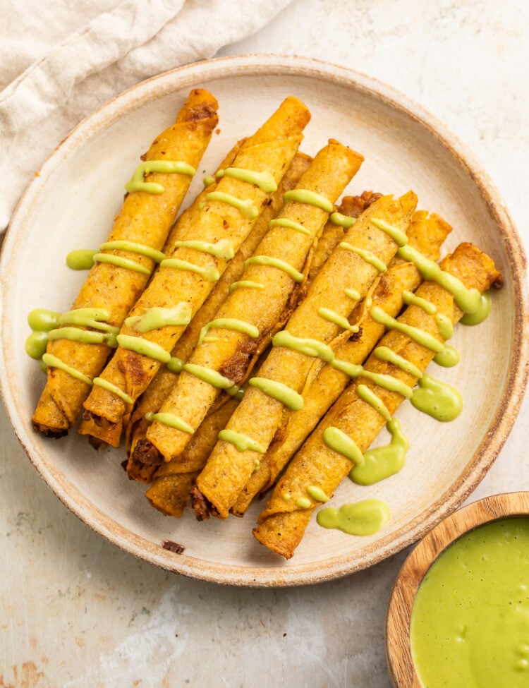 Overhead view of crispy frozen taquitos cooked in the air fryer on a plate, with a drizzle of avocado sauce.