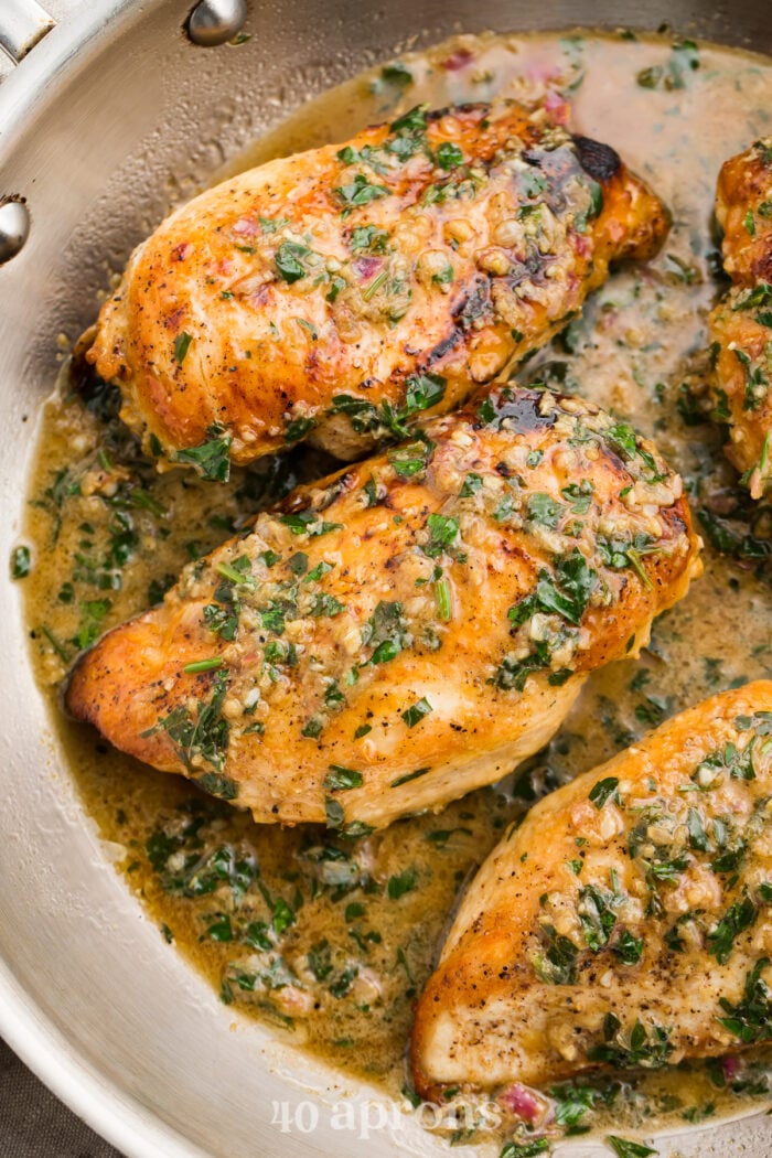 Overhead view of garlic herb butter chicken breasts in a large silver skillet.