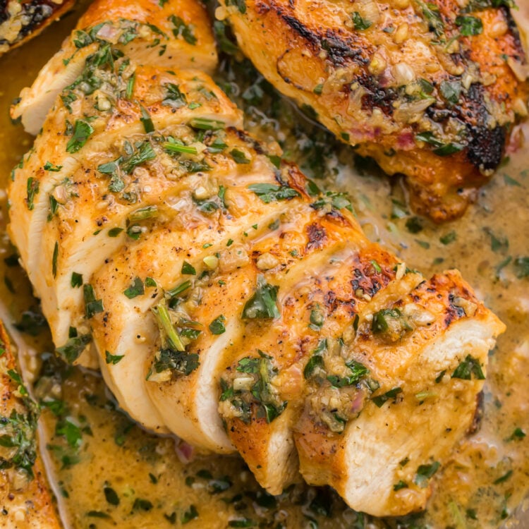 Overhead, close-up view of a sliced garlic herb butter chicken breast in garlic herb sauce in a large silver skillet.
