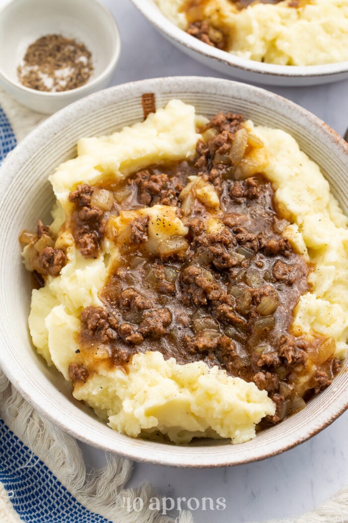 Angled, overhead view of a bowl of ground beef and gravy on top of fluffy, creamy mashed potatoes.