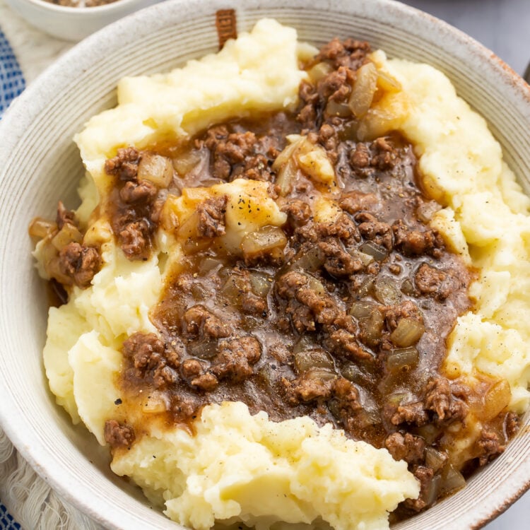 Angled, overhead view of a bowl of ground beef and gravy on top of fluffy, creamy mashed potatoes.