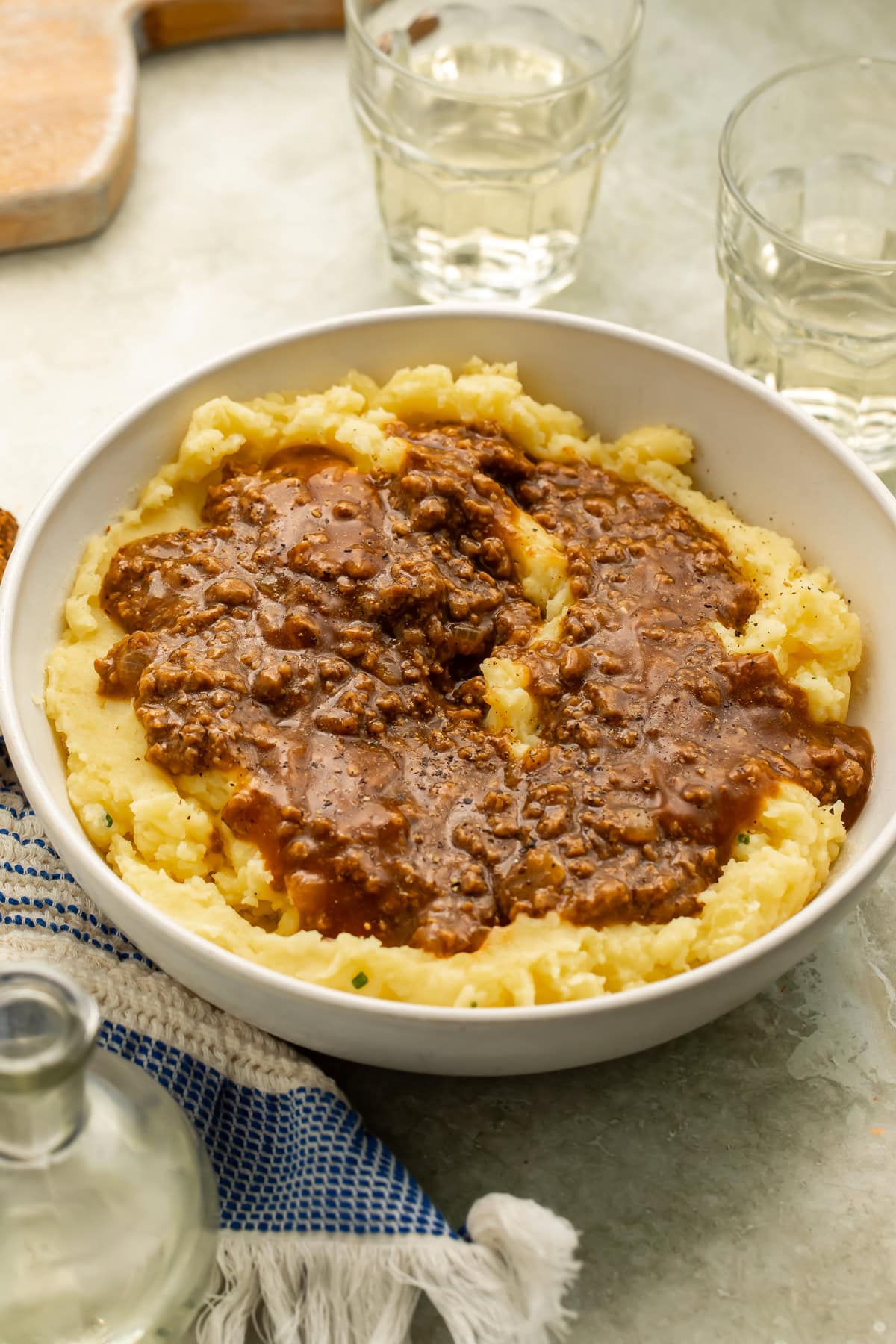 Bowl of mashed potatoes, ground beef and gravy with glasses of wine in the background.