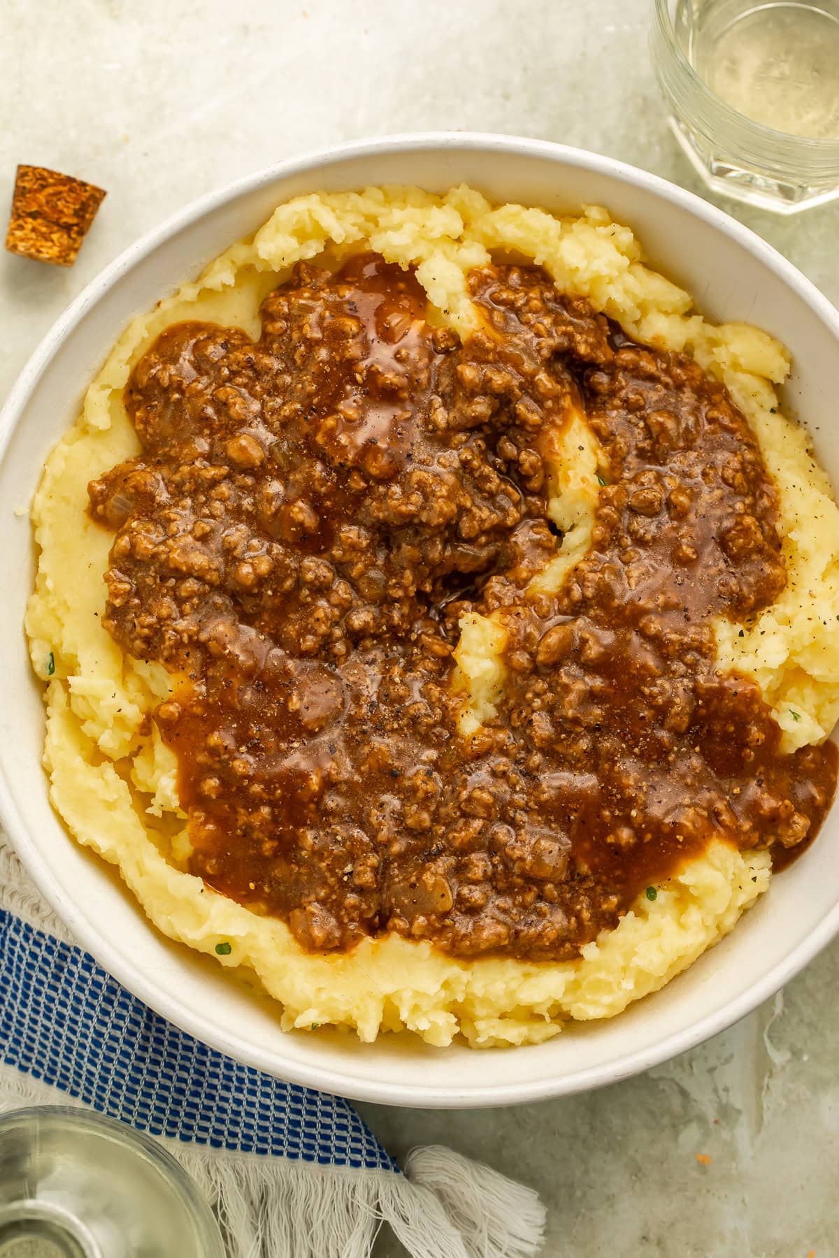 Overhead image of a bowl of mashed potatoes topped with ground beef in gravy.