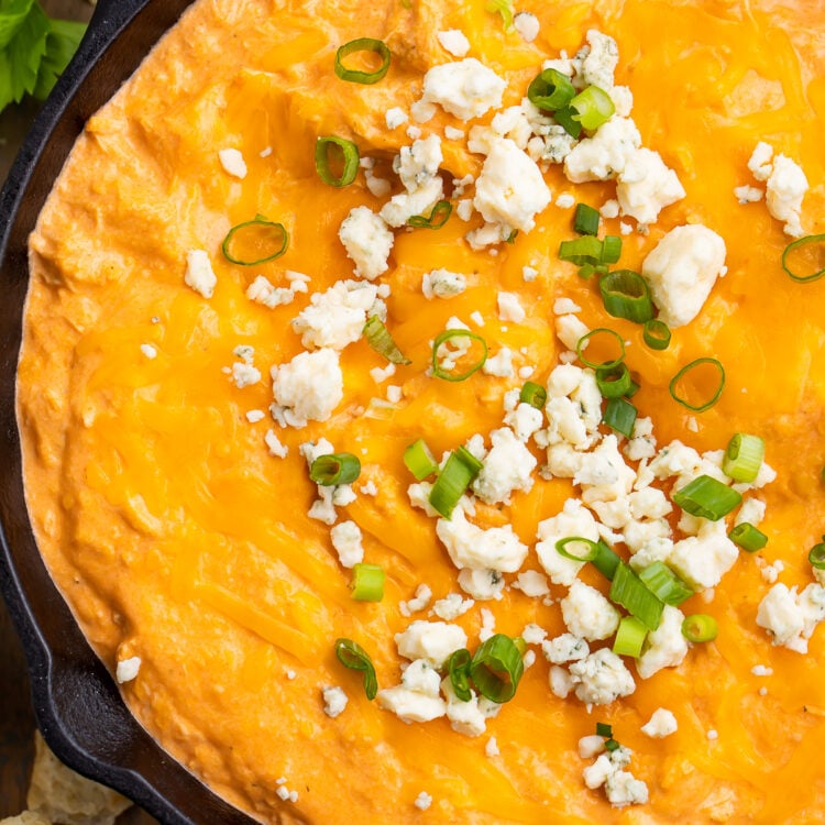 Overhead view of Instant Pot buffalo chicken dip in a cast-iron skillet. Dip is topped with blue cheese crumbles and green onions.