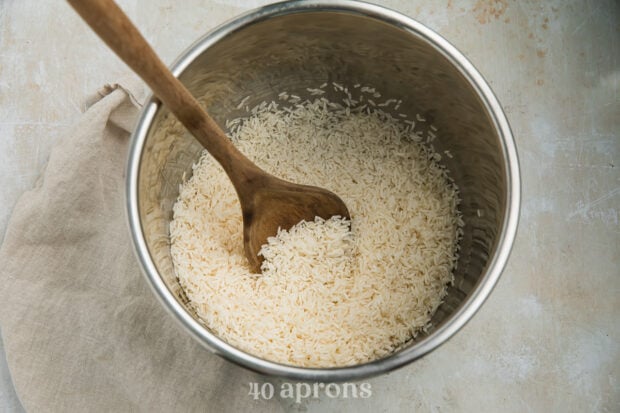 Overhead view of long grain rice in the Instant Pot insert with a wooden spoon.