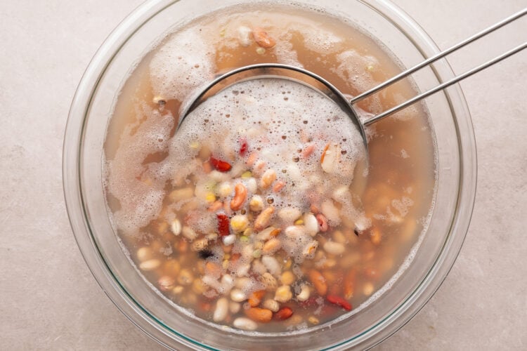 Overhead view of rinsed dried 15 bean soup in a large glass bowl with a fine mesh strainer.