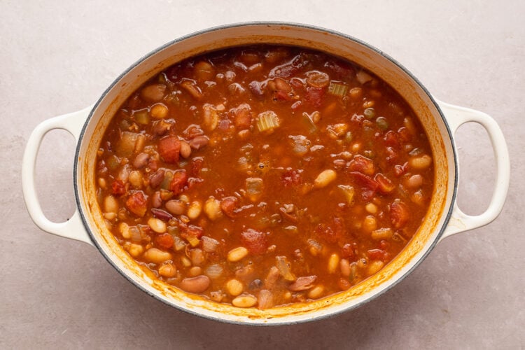 Overhead view of 15 bean soup with beans, bacon, onion, celery, tomatoes, and spices in a large oval pot with 2 handles.