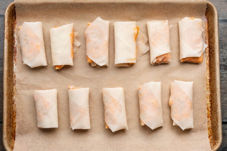 Overhead view of rolled and sealed buffalo chicken egg roll wrappers on a baking sheet lined with parchment paper.
