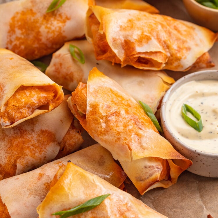Overhead view of buffalo chicken egg rolls on a sheet of parchment paper next to a ramekin of ranch dressing.