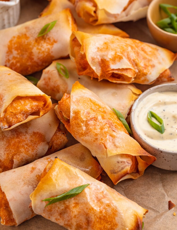 Overhead view of buffalo chicken egg rolls on a sheet of parchment paper next to a ramekin of ranch dressing.